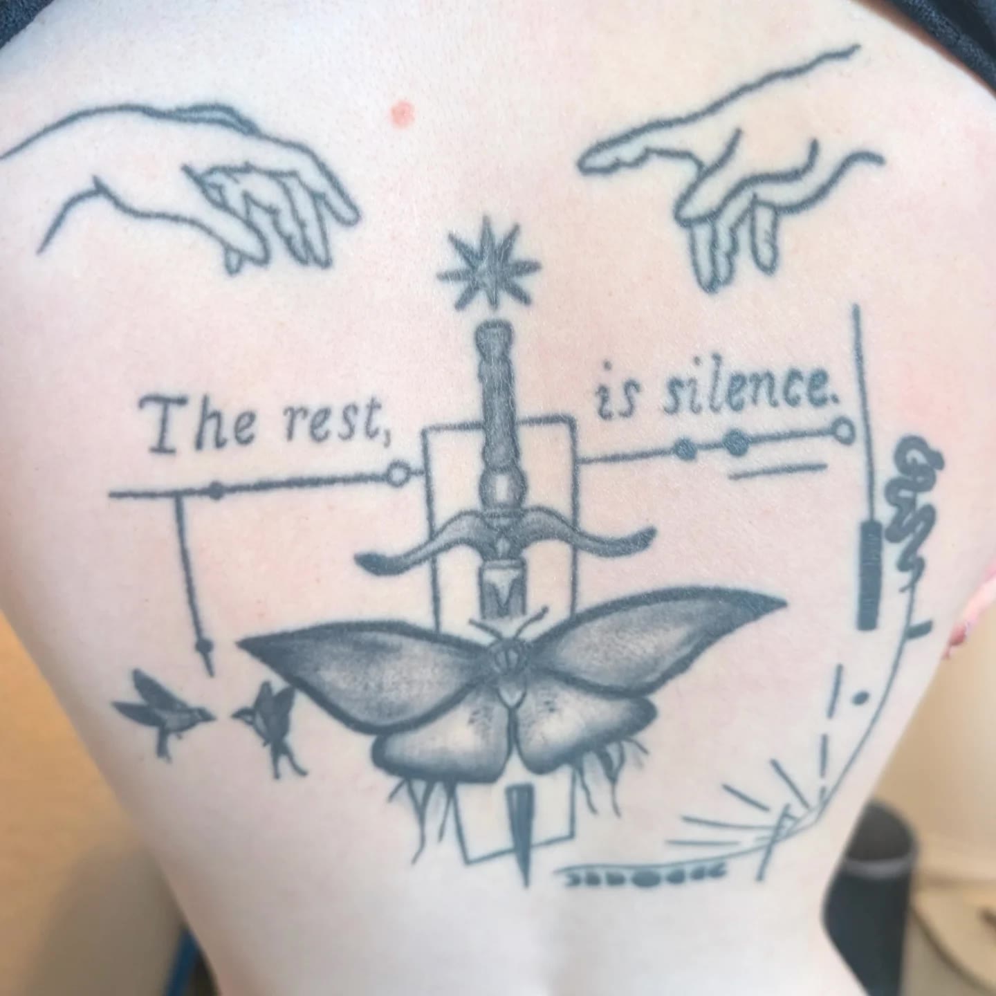 Finished black line tattoo with a butterfly, birds, and lettering.