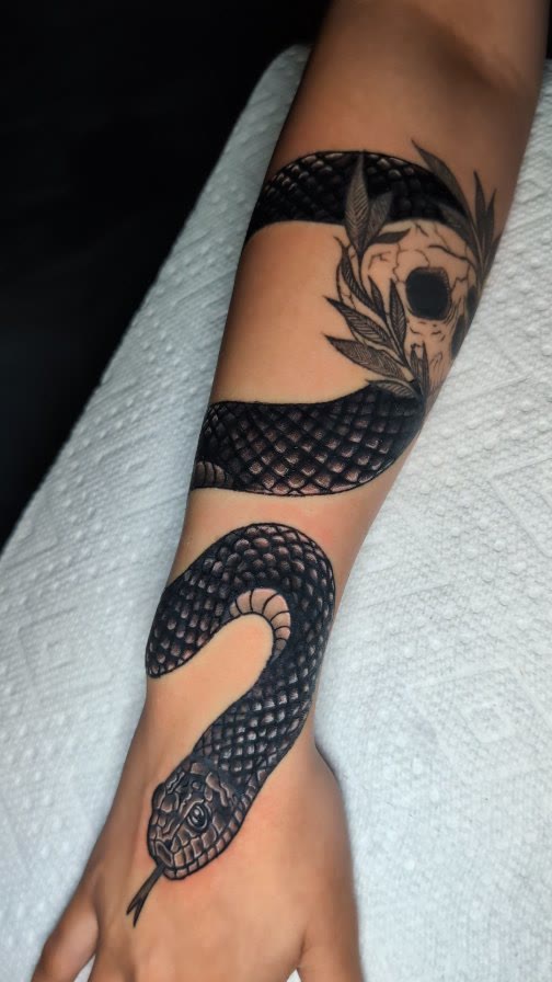 Black and grey snake tattoo on a forearm and hand.